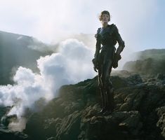 a woman standing on top of a rocky mountain next to steam rising from the ground