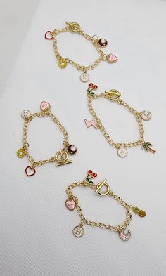 three different types of bracelets on a white surface with hearts and other charms attached to them