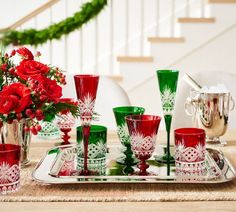 a tray topped with red and green glassware on top of a wooden table next to flowers