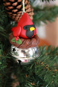 a red bird ornament hanging from a christmas tree with pine cones in the background