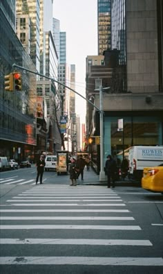 people are crossing the street in front of tall buildings on a city street with traffic lights