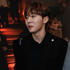 a young man in a black shirt and blazer looking off into the distance while standing next to stairs