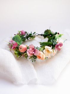 a flower crown is sitting on top of a white cloth with green leaves and pink flowers