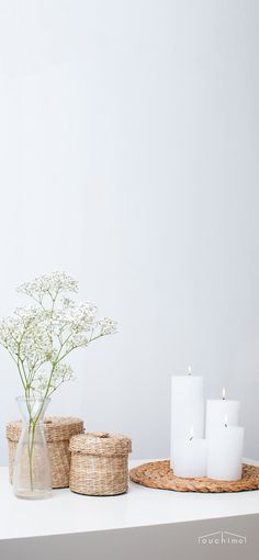 three white candles are sitting on a table next to baskets with flowers and vases