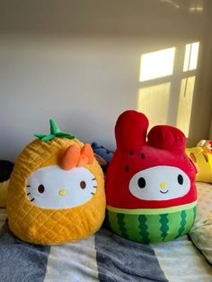 two hello kitty pillows sitting on top of a bed next to an orange and pineapple pillow