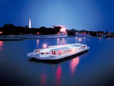 a white boat floating on top of a river next to a bridge at night with the washington monument in the background