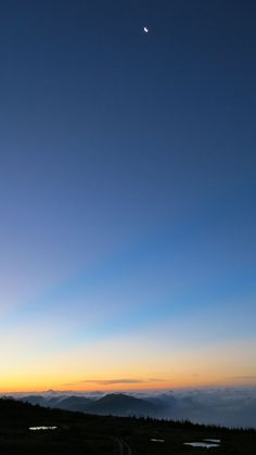 the sun is setting over some hills and water in the distance, with a plane flying overhead