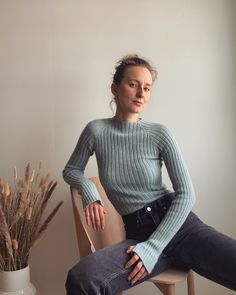 a woman sitting in a chair next to a potted plant and wearing a sweater