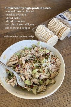 a bowl filled with salad next to crackers on top of a wooden table in front of a bag of chips