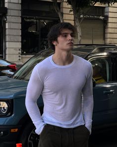 a young man standing in front of a car on the street with his hands in his pockets