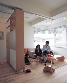 two people sitting on a couch in a room with wood flooring and white walls