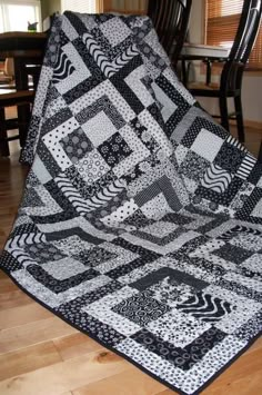 a black and white quilt sitting on top of a wooden floor next to a chair