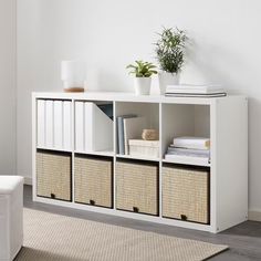 a white shelf with baskets and plants on top in a room next to a couch