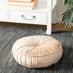 a round ottoman sitting on top of a rug next to a white table and drawers