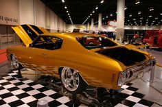 an orange muscle car on display in a museum with black and white checkered flooring