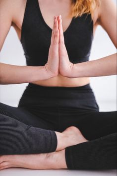 a woman sitting in a yoga pose with her hands folded out to the side while wearing a black tank top and leggings