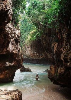 a person wading in the water between two large rocks on either side of a river