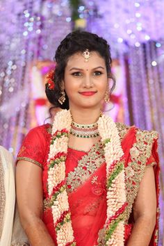 a woman in a red and white sari standing next to a wall with lights