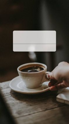 a person holding a cup of coffee on top of a wooden table next to a laptop