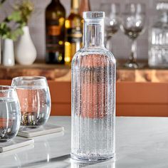 a glass bottle sitting on top of a counter next to two wine glasses and bottles