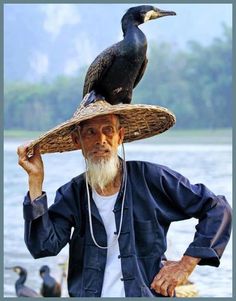 an old man with a bird on his head standing in front of some water and ducks