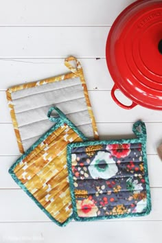 two pot holders are sitting next to each other on the table, one has a red lid