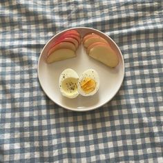 sliced apples and an egg on a plate with blue checkered tablecloth, ready to be eaten