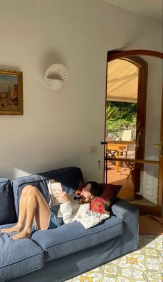 a woman laying on top of a blue couch in a living room next to a doorway