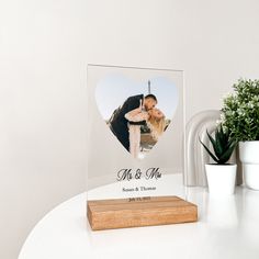 an acrylic photo frame with a wooden stand on a table next to a potted plant