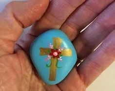 a hand holding a small blue rock with a cross painted on it's side