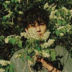 a person standing in front of some white flowers and green leaves with their hands on his face