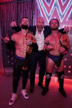 three men standing next to each other holding up their wrestling belts