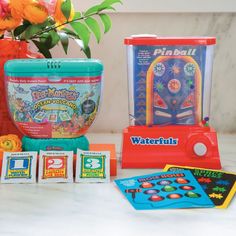 an assortment of toys and games sitting on a table next to a vase with flowers