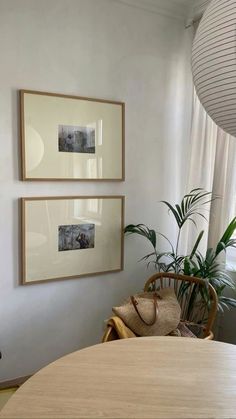 two framed pictures hang on the wall above a dining room table with chairs and a wicker basket