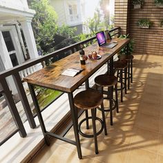 a long table with four stools and a laptop on it in front of a balcony