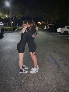 two young women hugging each other in the middle of an empty parking lot at night