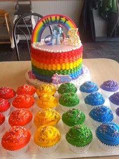 there are many cupcakes on the table and one has a rainbow frosted cake