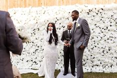 a man and woman standing next to each other in front of a flower covered wall