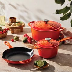 pots and pans are sitting on a table next to each other, including one with an orange lid