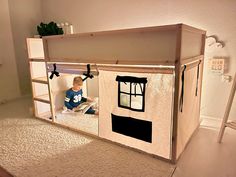 a child sitting on the floor in front of a doll house made out of cardboard