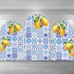 three yellow lemons on blue and white tiles with green leaves in the middle, against a brick wall