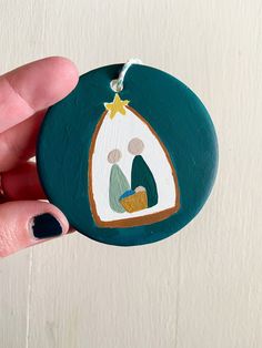 a hand holding a christmas ornament with a nativity scene painted on it