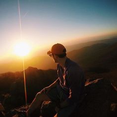 a man sitting on top of a mountain with the sun setting in the sky behind him