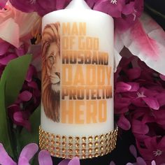 a white candle with the words man of god and a lion on it surrounded by purple flowers