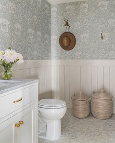 a white toilet sitting in a bathroom next to two baskets with flowers on top of it