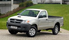 a silver truck parked in front of a building on the side of a road with grass and bushes behind it