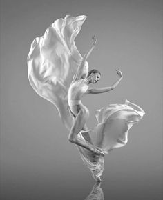 a black and white photo of a ballerina in the air with her dress flowing