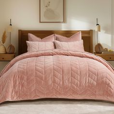 a bed with pink comforter and pillows in a bedroom area next to two nightstands