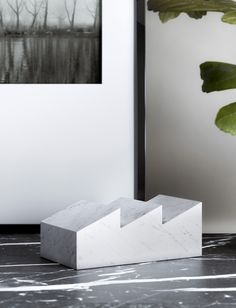 a white marble block sitting on top of a table next to a green leafy plant