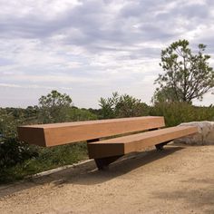 two people sitting on a bench near some rocks and trees in the distance, with one person pointing at something